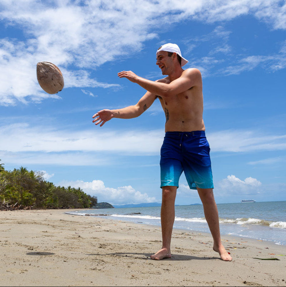 Man on a beach throwing a coconut against a blue sky