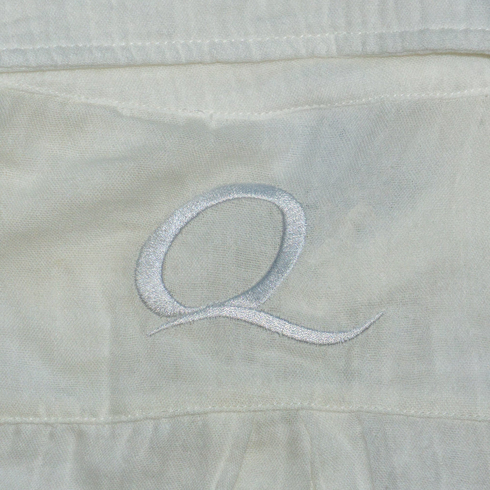 Close-up of a light-colored fabric with an embroidered letter 'Q'.