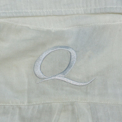 Close-up of a light-colored fabric with an embroidered letter 'Q'.